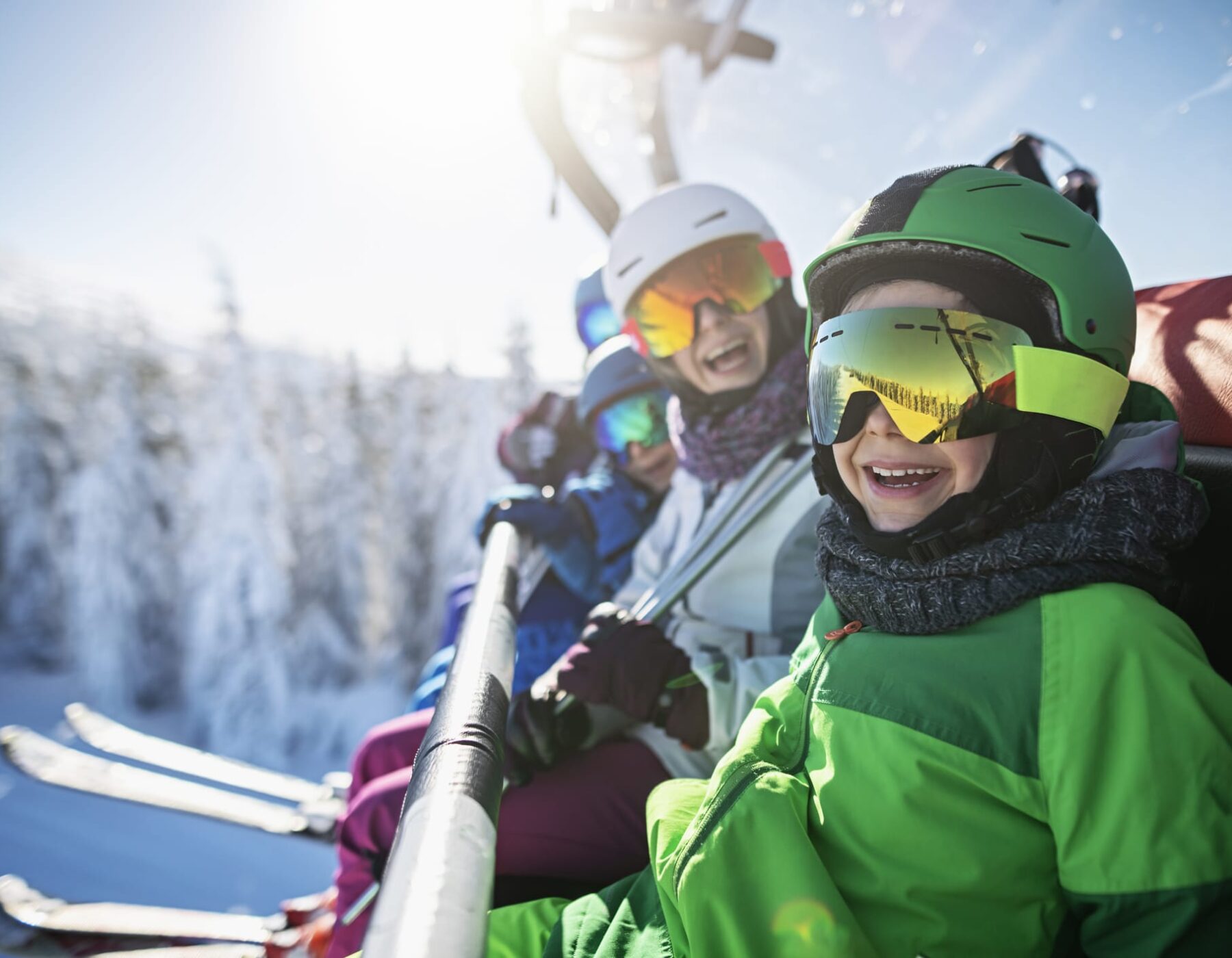 Mother skiing with kids on a sunny winter day. Family is sitting on chairlift cheering at the camera.
Nikon D850